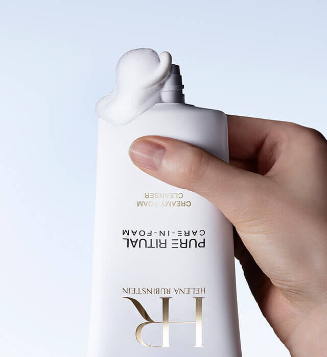 Una mano stringe un flacone di Pure Ritual Care-in-Foam di Helena Rubinstein, dal quale fuoriesce una quantita di prodotto.