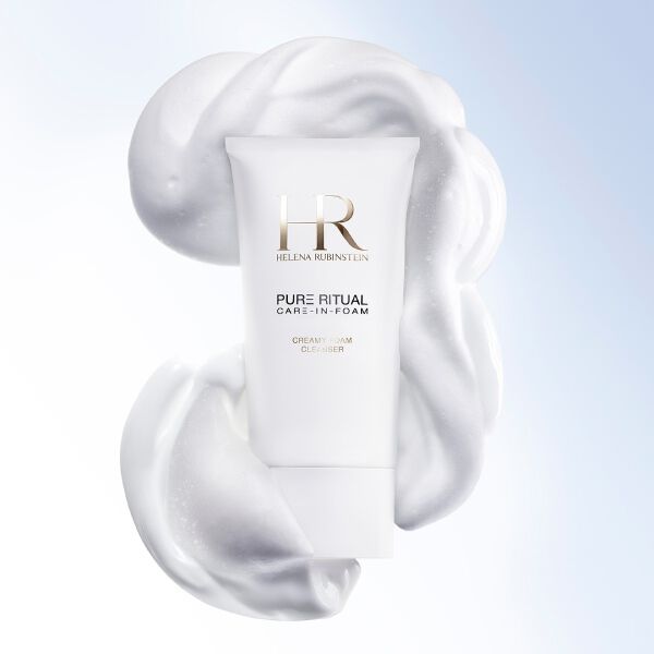 Primo piano del detergente Pure Ritual Care-in-Foam di Helena Rubinstein circondato da una soffice schiuma bianca, accanto al volto di una donna dall'incarnato puro e luminoso.​