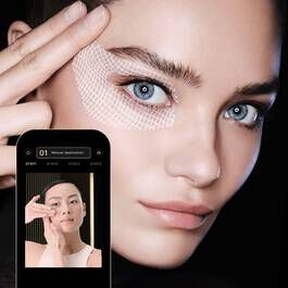 Modella con pelle perfetta e occhi blu, mentre usa un\'app per il trucco sullo smartphone.