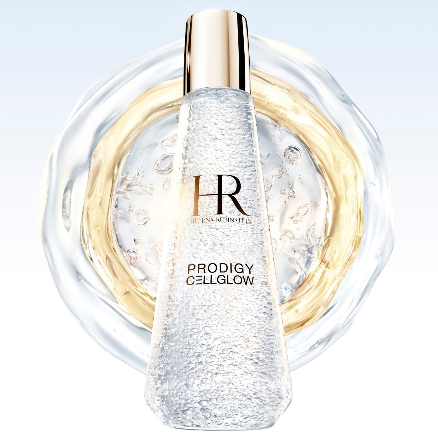  Flacone di siero "Helena Rubinstein Prodigy Cellglow" riempito di bolle, al centro di anelli liquidi traslucidi e dorati che si estendono su uno sfondo chiaro.